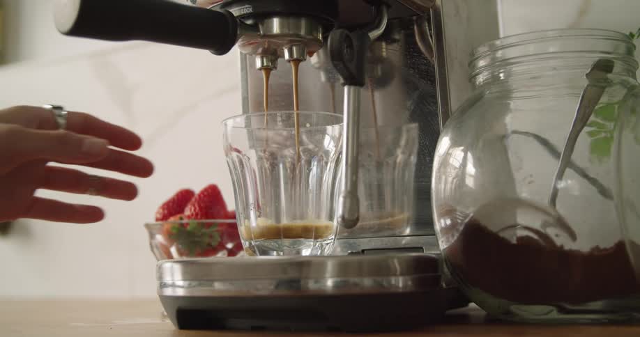 A machine is making espresso in a glass as a hand reaches for it
