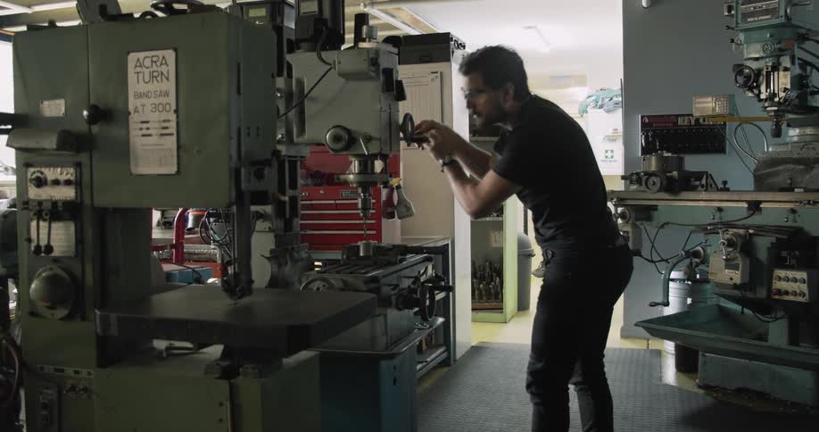 A man in a shop uses a drill press
