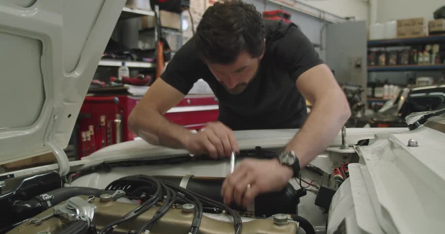 A man works under the hood of his car in his garage