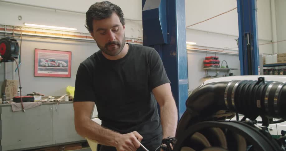 A man in a garage with a tool working on an engine