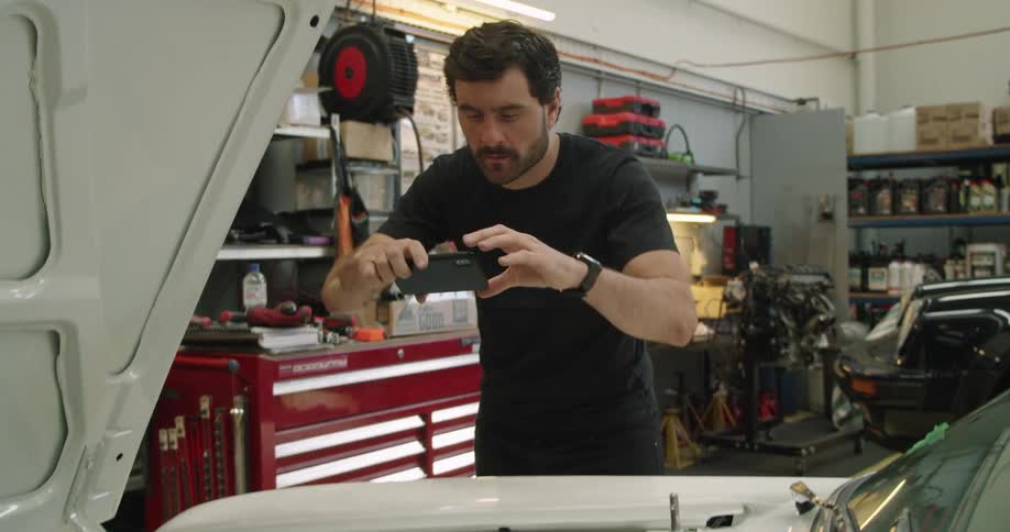 A man takes a picture of the engine of a vehicle inside an auto repair shop