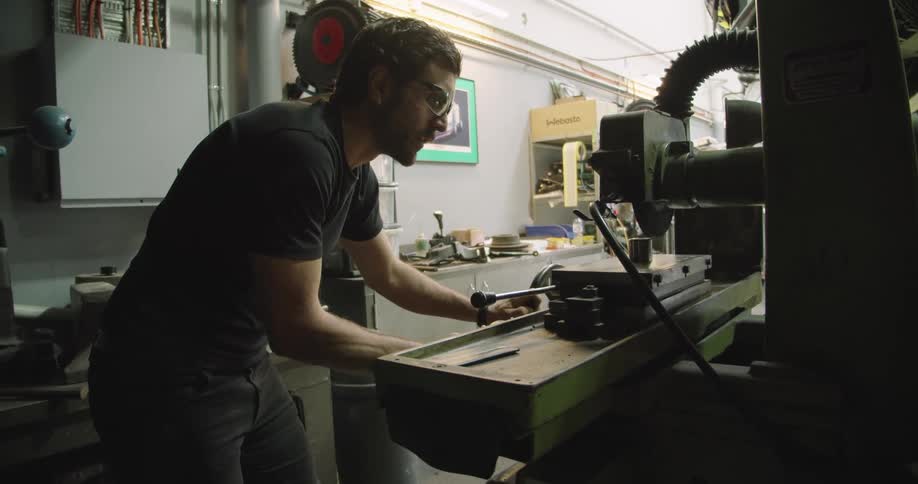 A man in a workshop cutting a piece of metal with a saw