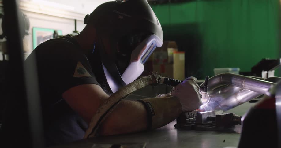 A man with a welding mask and gloves welding a piece of metal