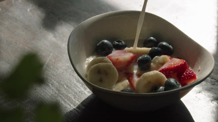 Pouring milk over bananas and berries in a white bowl