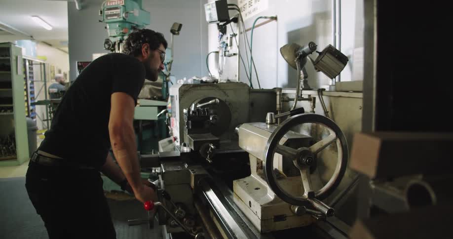 Man using a lathe to shape a piece of metal on a workshop