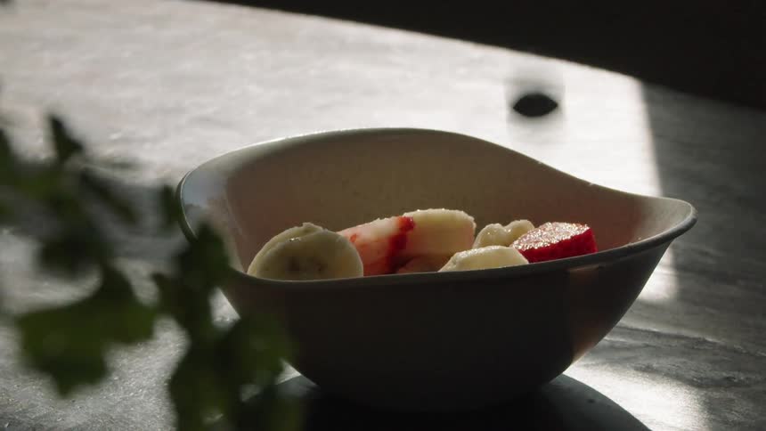 Fruit falling over a fruit salad inside a wooden bowl in a table at home