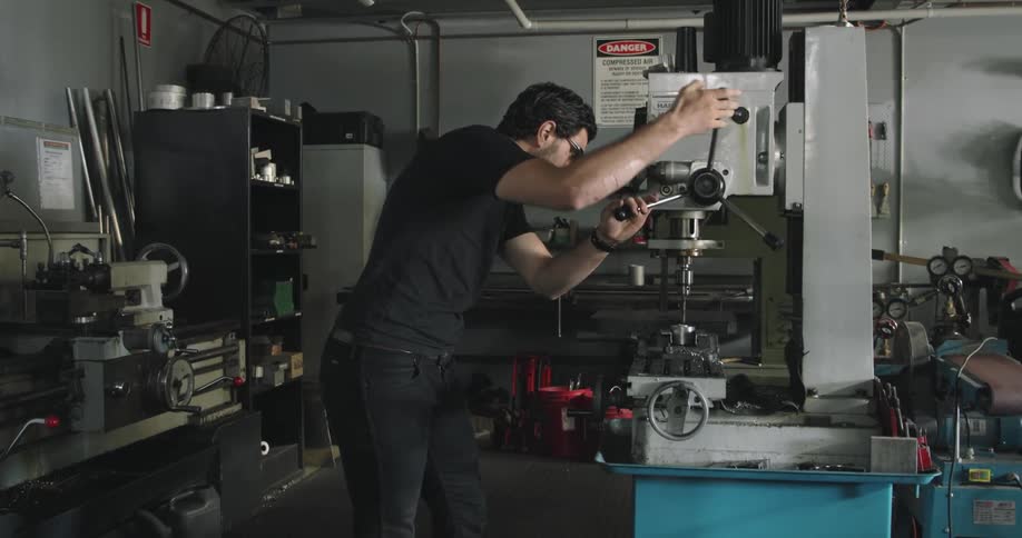 Man drilling metal with a drill on a workbench in a workshop