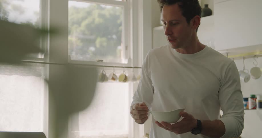 A man in a room video chatting on a laptop while eating a bowl of fruit