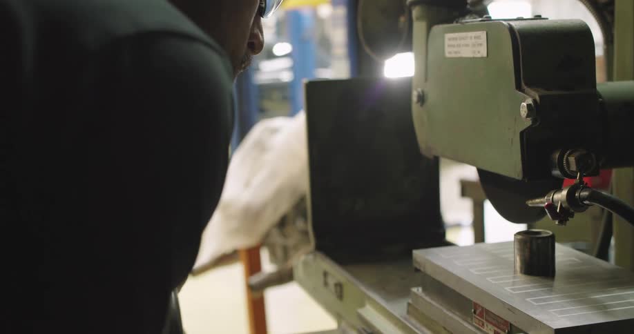 A man in a workshop cutting a piece of metal with a saw