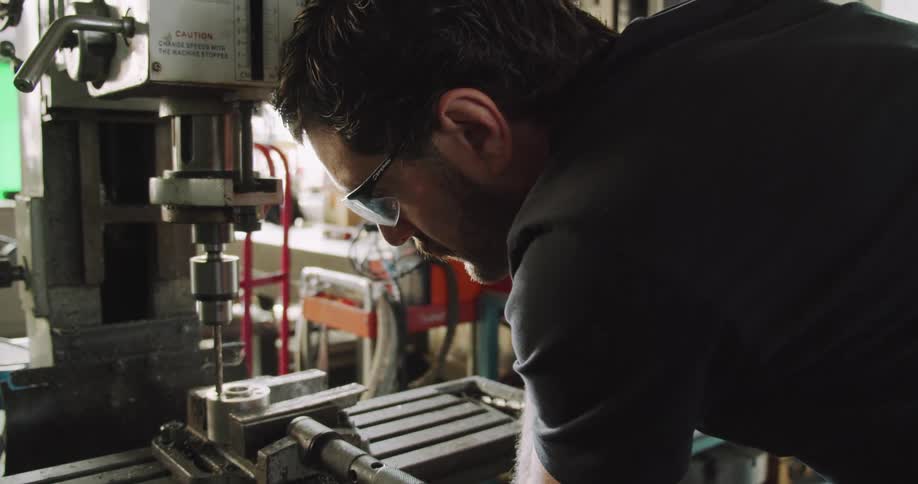 A man uses a large machine to drill a hole in something inside a workshop