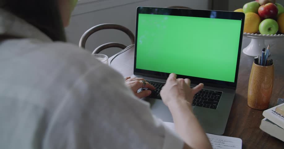Woman with long hair and white shirt works on apple macbook laptop in the kitchen