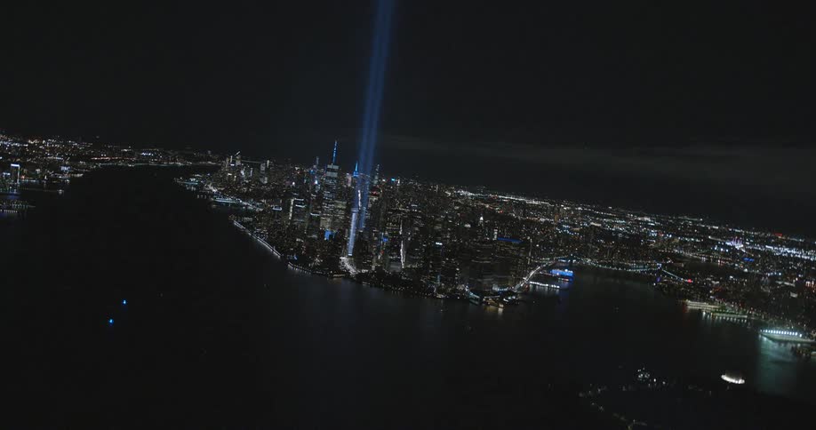 Two tall vertical beams of blue light shoot up from a downtown building along the water