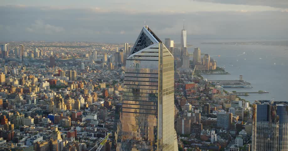 A group of people on a triangular balcony near the top skyscraper looming over the buildings on the coast of a metropolis during the day