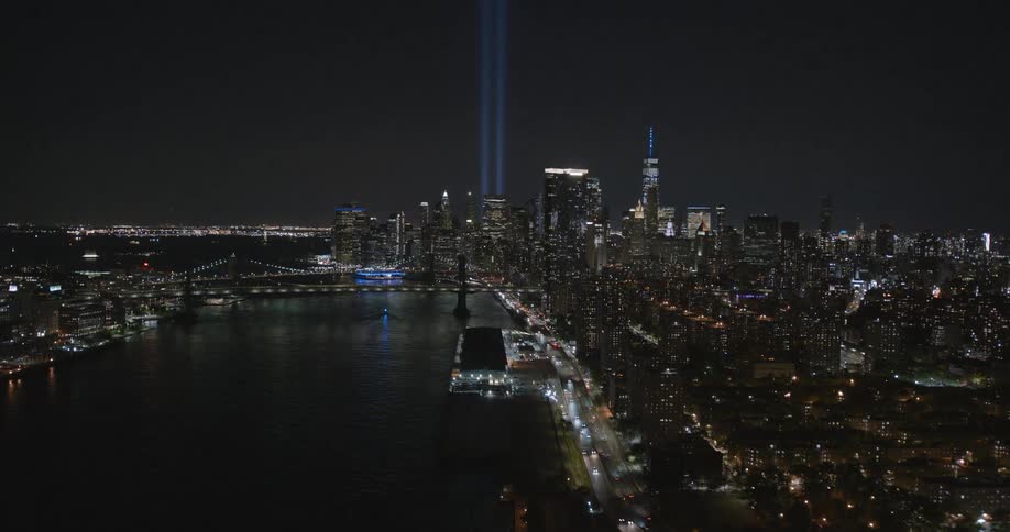 Two pillars of light reach into the night sky over a metropolis and the river running through it