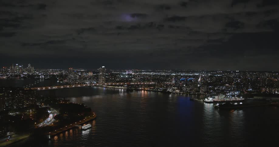 A nighttime view of a city in lights with a body of water and a bridge