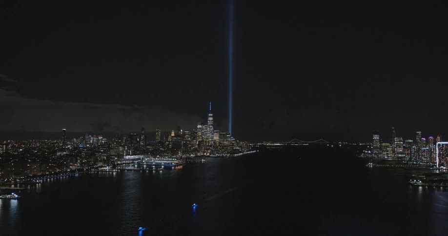 A tall vertical blue light shoots up through the sky from downtown near a river