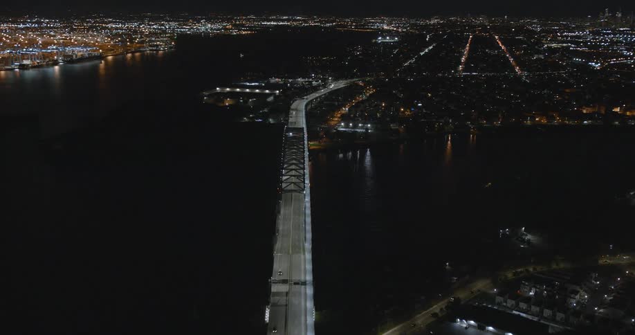 An aerial view of cars driving across a bridge and a lit of city skyline