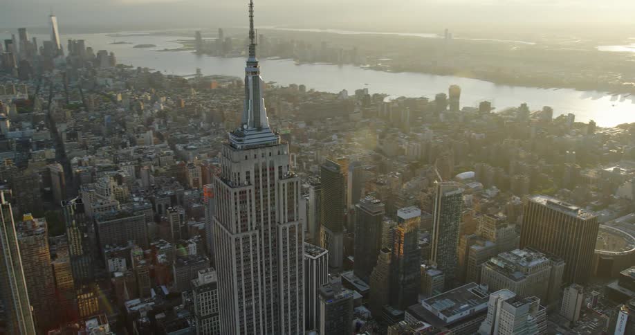 An aerial view of new york city with many buildings against a body of water with sunlight