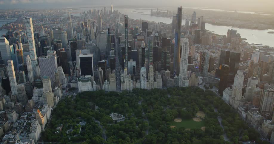 A large public park surrounding by skyscrapers in a metropolis during the day
