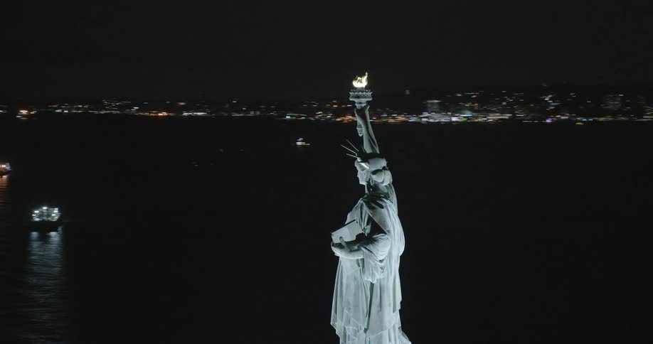 An aerial view of boats floating around the statue of liberty at night