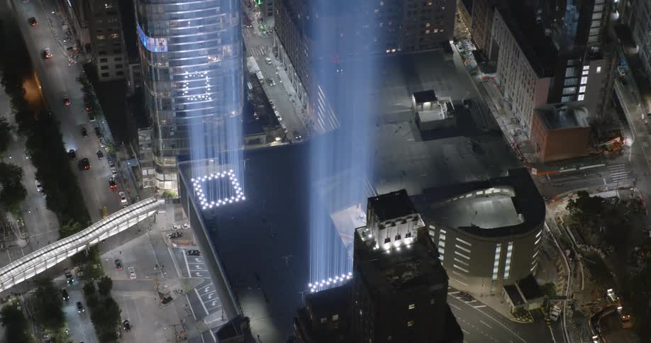A nighttime shot of the 911 memorial with surrounding buildings and streets with traffic