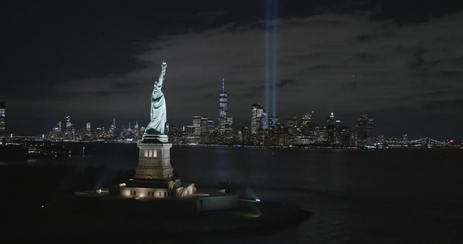 The statue of liberty sculpture on liberty island in front of the tribute in light in manhattan at night