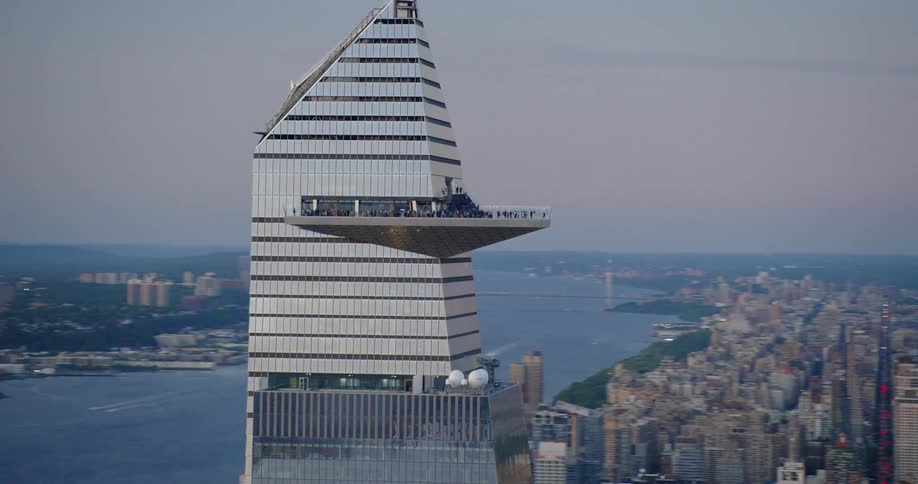 Aerial view of a silver building with a triangular balcony with people against a body of water in a city area