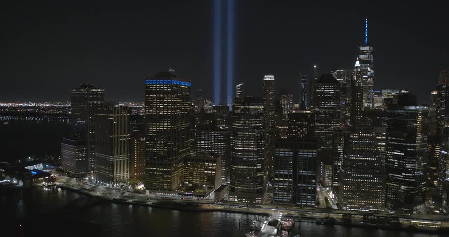Aerial view of lit up skyscrapers at night with cars driving along the coast and boats in the water