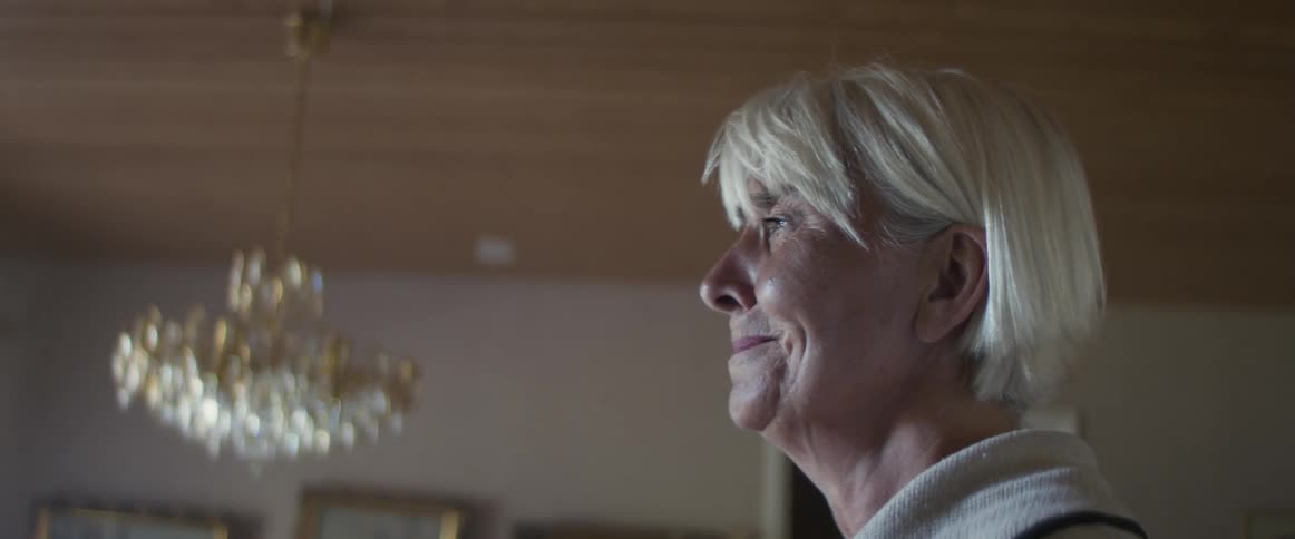 Side view of an elderly woman standing and crying while looking out the window in dining room