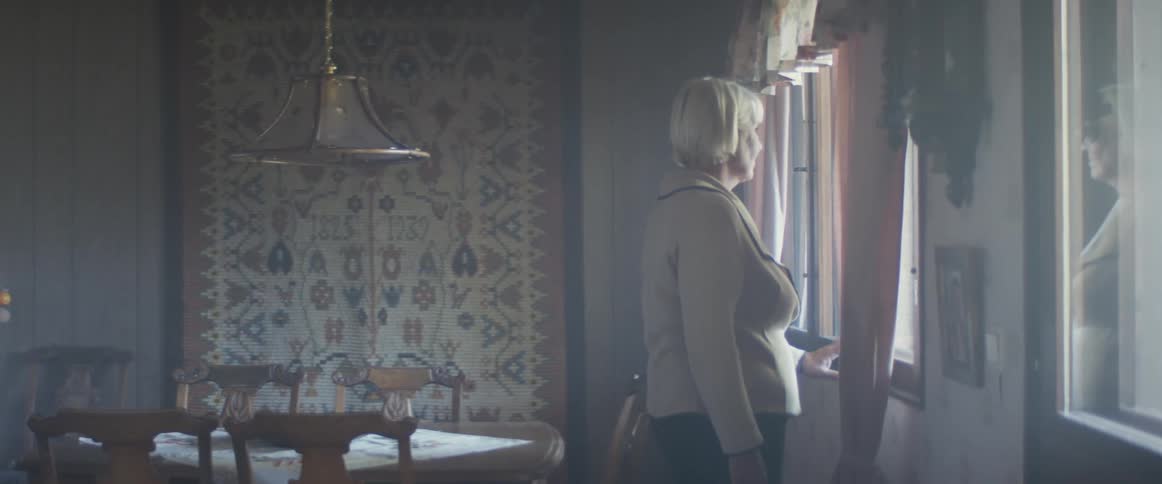 A woman walks from her kitchen and across her living room to look out a window