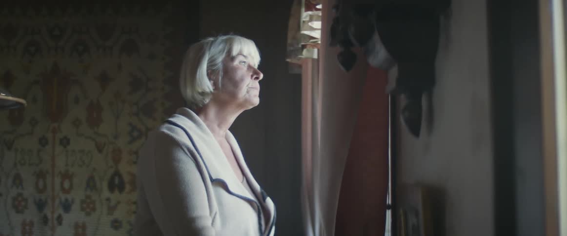 Senior woman attentively looks out of the window from a dimly lit room