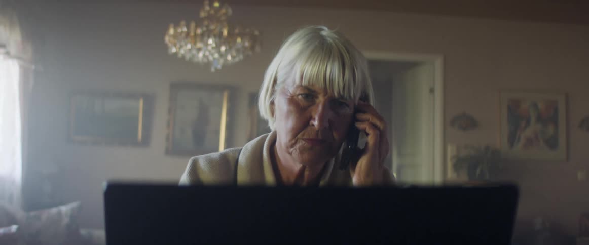 A woman is sitting in a house and talking on the phone