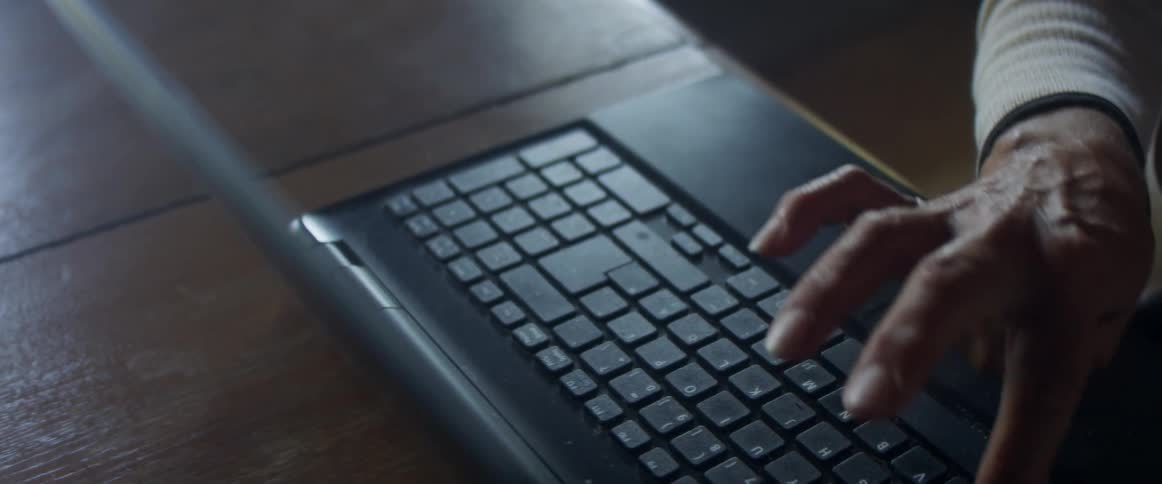 Elderly womans hand types on laptop keyboard