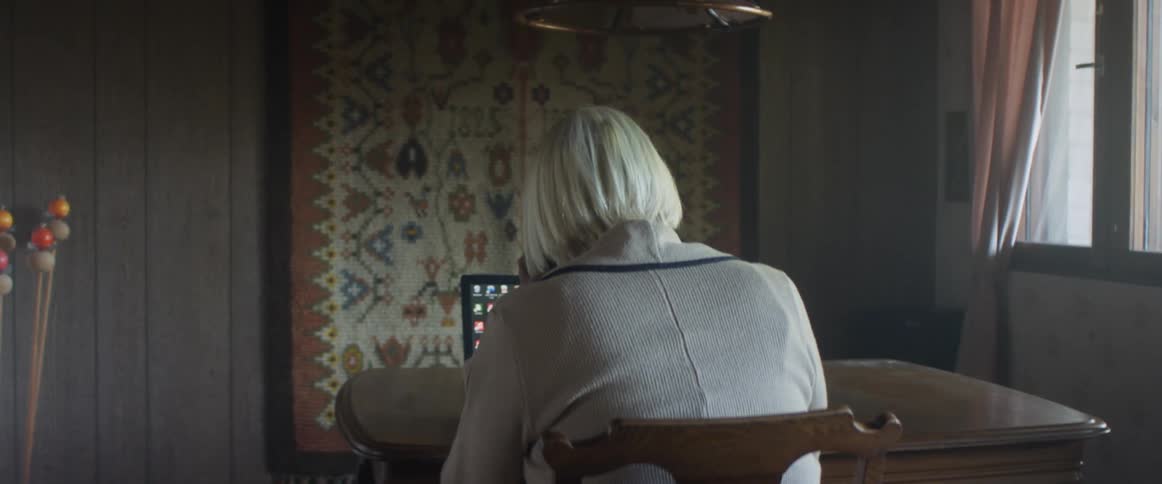 Elderly woman with grey hair sitting at a table uses a laptop in a room