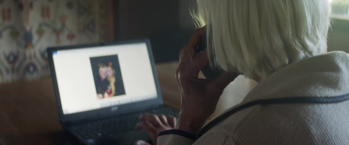 A woman sits at a laptop and desk talking on a cell phone