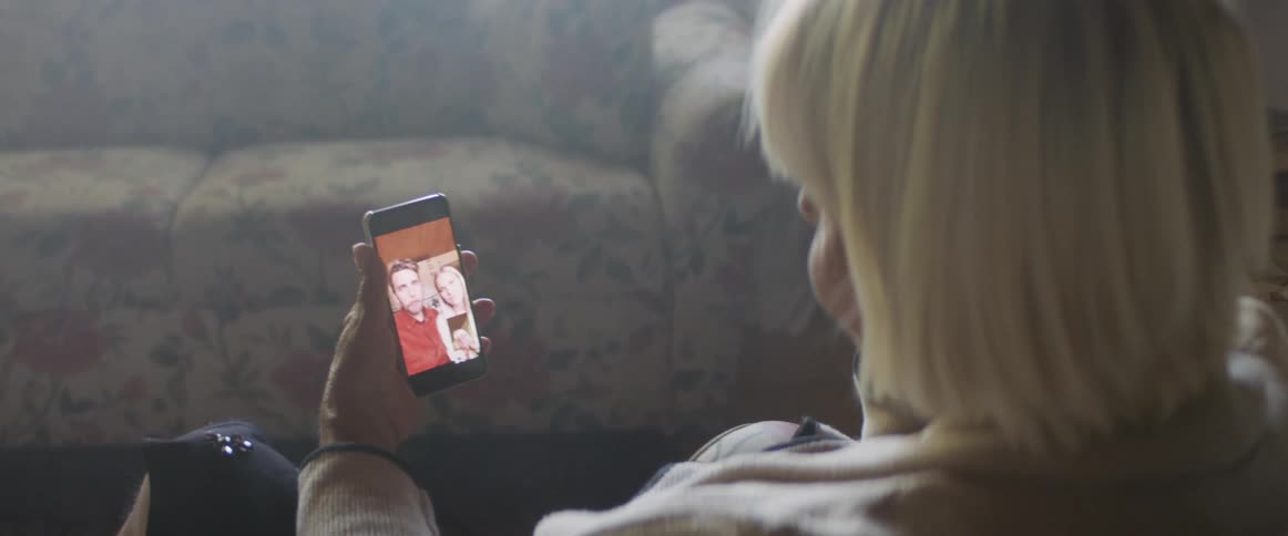 Elderly woman sitting in an armchair makes a video call on smartphone in living room at home