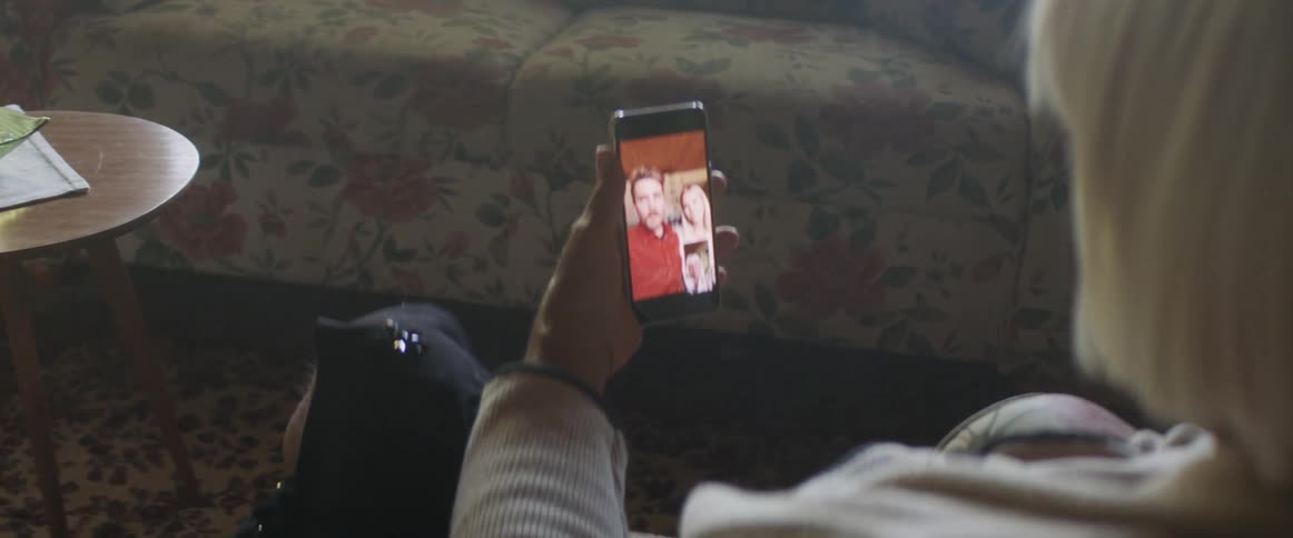 Elderly woman with grey hair sits in an armchair makes a video call on a smartphone in living room at home