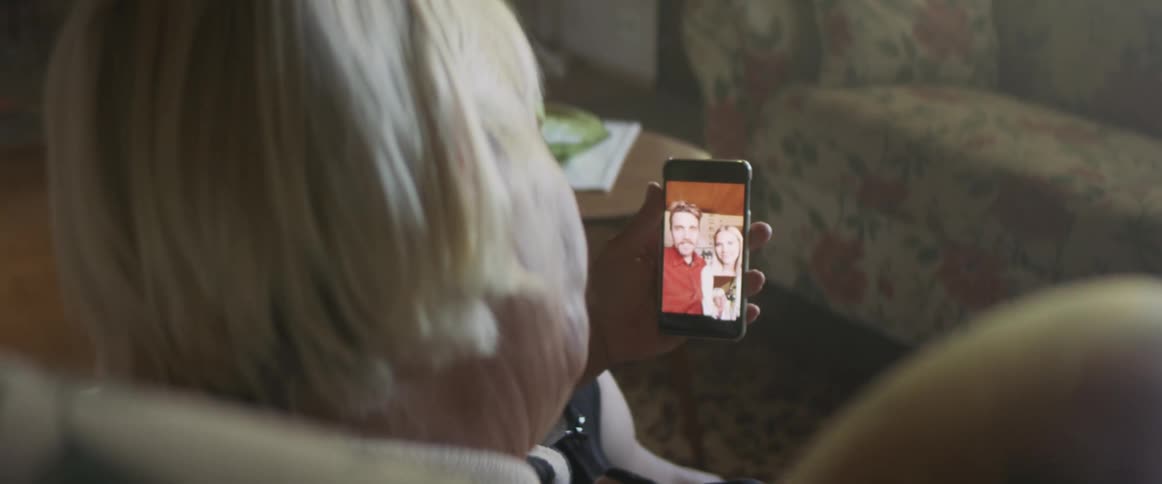Elderly woman sitting in armchair makes a video call on smartphone in living room at home