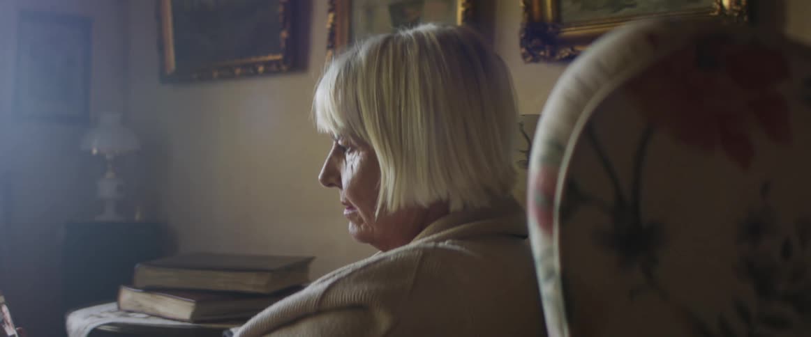 Woman with grey hair sitting in an armchair makes a video call on a smartphone in living room at home