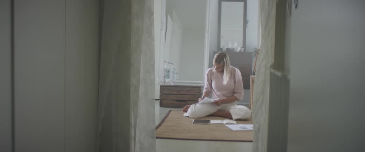 A woman sits on the floor with several papers and a pen