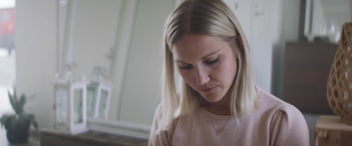 Blonde woman with white pants and a pink sweater sits on the ground and writes things down in a notebook in living room at home