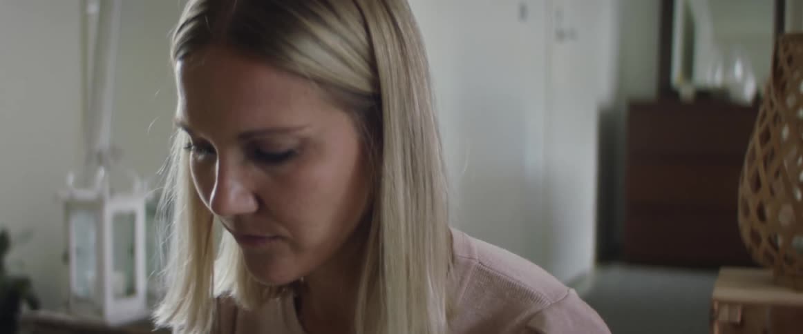 Blonde woman with a pink sweater looks down in living room at home