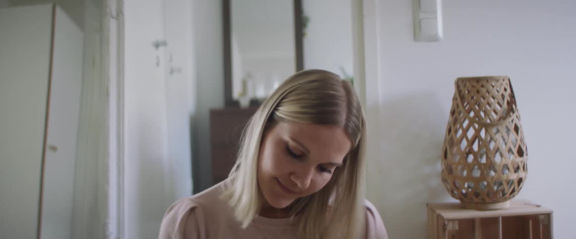 Woman with a pink sweater and white pants sitting on the ground writes things down in a notebook