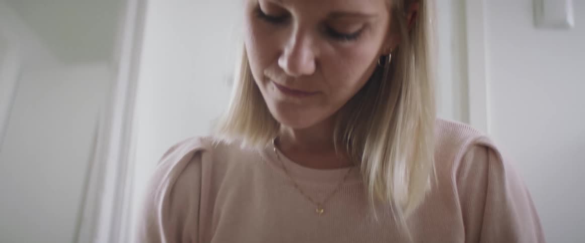 Blonde woman with a pink sweater and a white pants sits on a rug and writes things down in a notebook