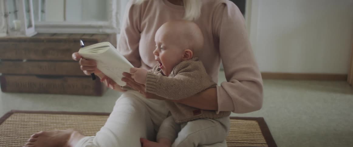 Mother holds baby and tries to write as baby keeps reaching for notebook