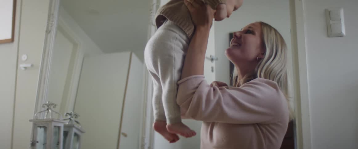 A woman lifts and plays with a baby indoors during the day