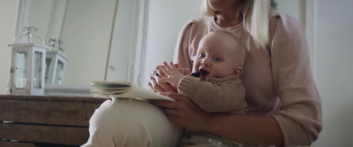 A woman holding a baby a pen and a pad with a mirror in the background