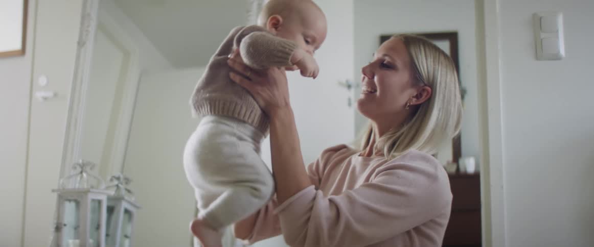 A woman lifts and smiles at a baby inside a house