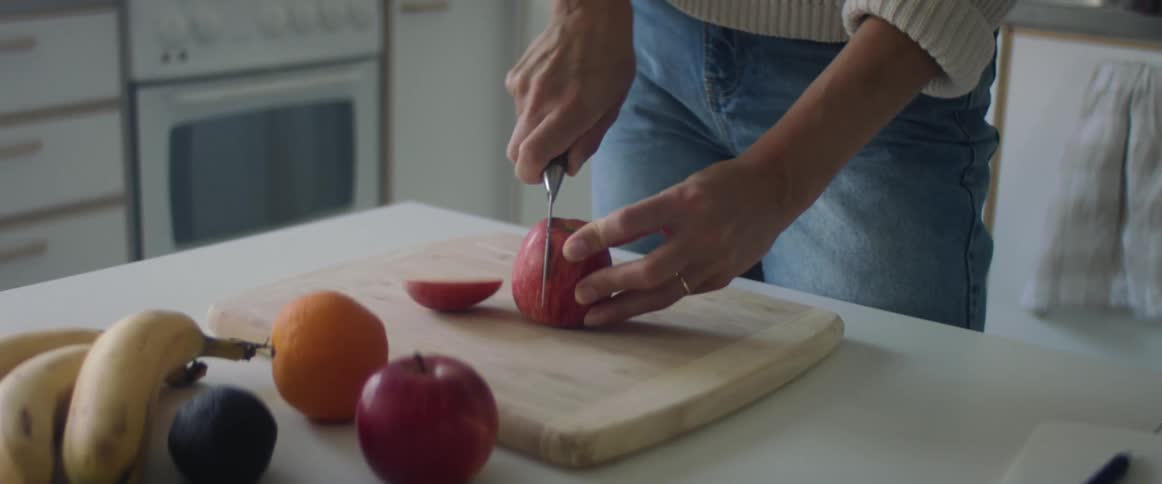A woman slicing an apple on a wood cutting board in a home kitchen
