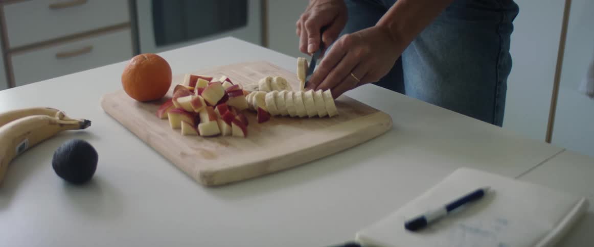 Woman slices fruit on wooden chopping board set on white kitchen island